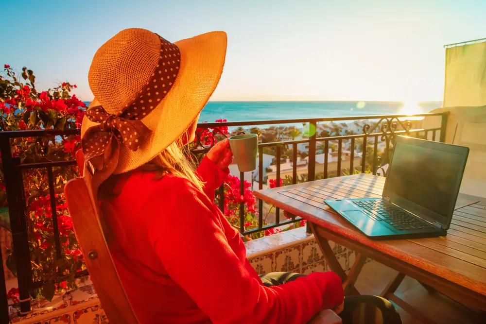 Remote worker with a laptop on a sunlit balcony overlooking the sea in Spain